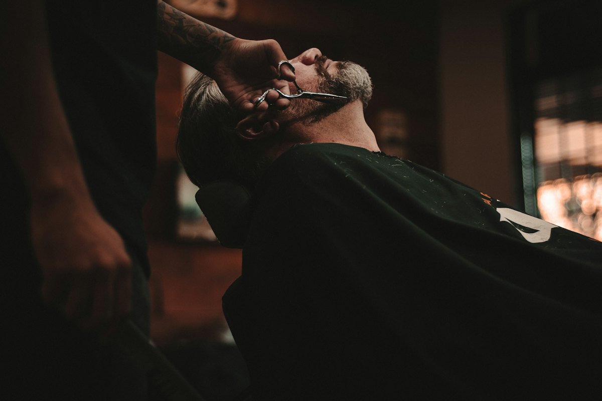 Barbeiro fazendo acabamento de barba em ambiente escuro